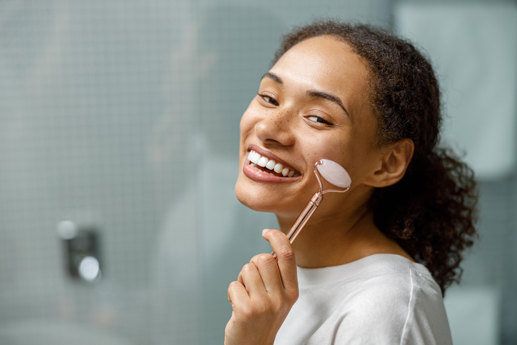 Smiling Woman making face massage using roller with quartz in bathroom. Natural cosmetics concept, zen care