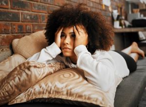 Depressed, sad and frustrated African woman thinking of idea with anxiety, problem with mental health and depression on the sofa in home. Frustrated, fear and tired girl with stress on house couch feeling guilt