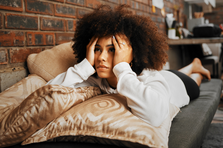 Depressed, sad and frustrated African woman thinking of idea with anxiety, problem with mental health and depression on the sofa in home. Frustrated, fear and tired girl with stress on house couch feeling guilt