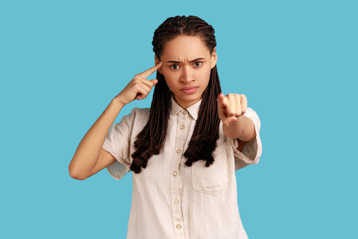 Woman shows stupid gesture, pointing to camera, blaming for insane plan, crazy idea, dumb suggestion