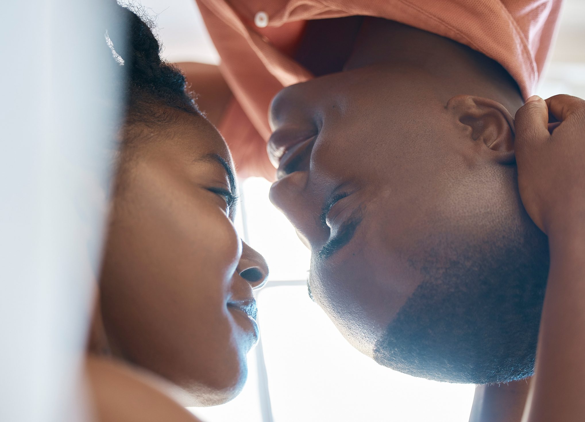 Sensual african american couple bonding and looking eye to eye while spending time together at home. Boyfriend leaning over his girlfriend lying on bed while relaxing together on the weekend exploring the g-spot