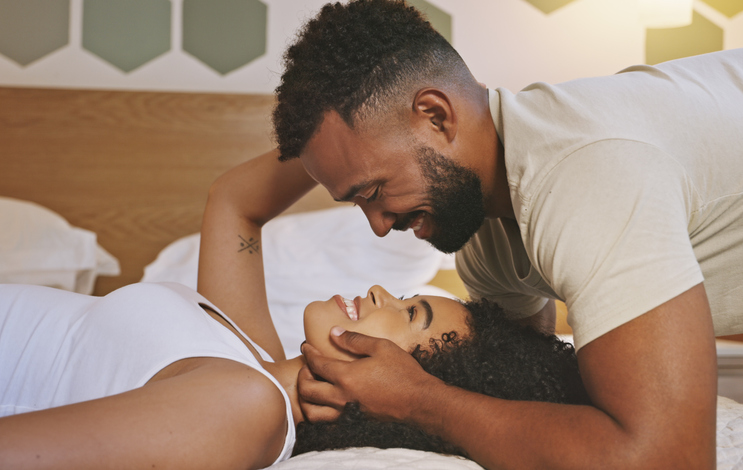 Faces of a loving young couple looking into each other's eyes while lying on a bed at home. Black boyfriend and girlfriend sharing a romantic moment expressing love and affection in the morning.