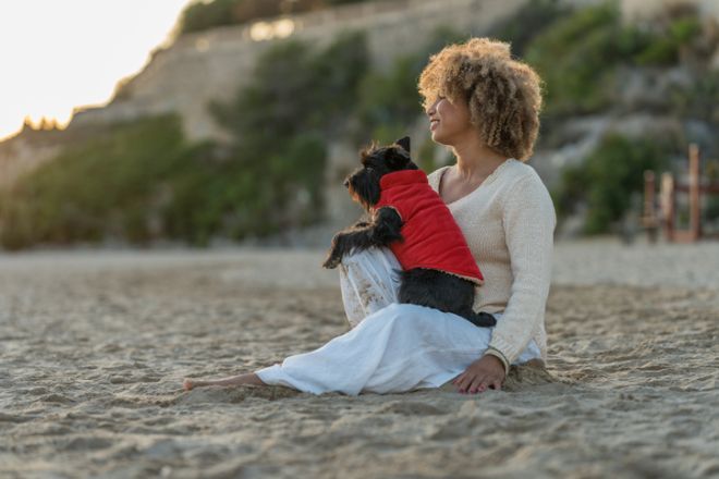 Woman sitting on the sand on the beach holding her puppy in her arms
