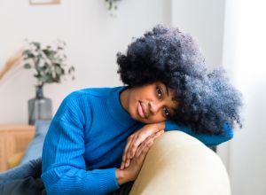 Cheerful black woman sitting on couch enjoying being selfish