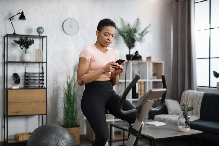 African female wearing sportswear writing message on her smartphone while working out