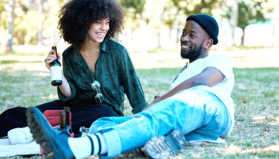 Interracial couple in nature park together, man and woman relax with drink on grass and happiness for people on picnic date outside. Happy black friends dating, laughing and having fun on weekend on valentine's day