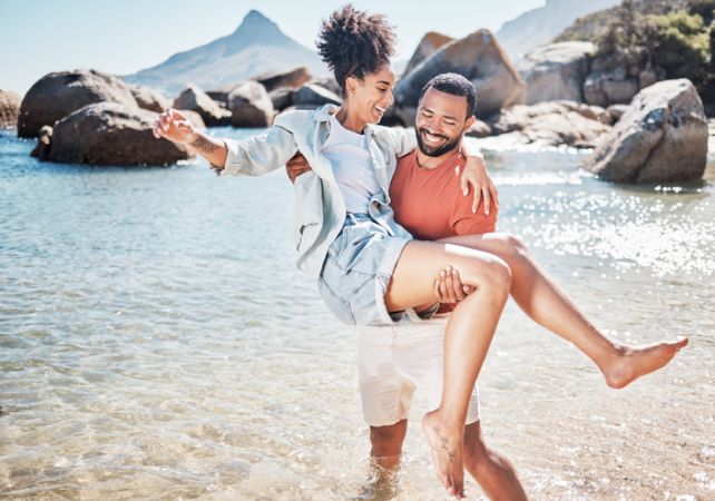 Couple, beach and man carrying woman for love, marriage support and funny holiday vacation. Travel, quality time together and summer freedom in Hawaii, sunshine and relax on ocean sand for happiness