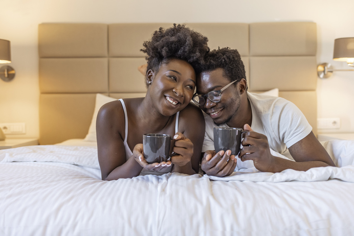 Affectionate couple enjoying morning coffee and cuddling in bed.