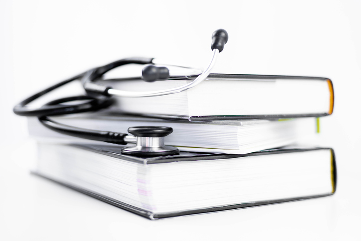 Side view of a stethoscope listening to stacked medicine books on a white background with copy space.