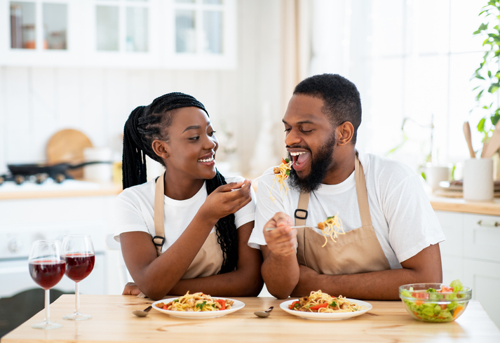 Happy Black Spouses Eating Lunch At Home, Enjoying Spaghetti And Wine good for penis health