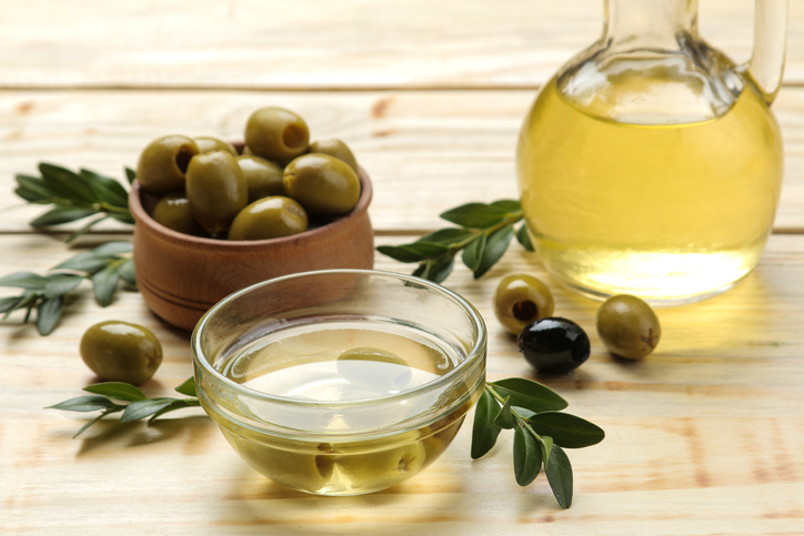 green olives with leaves in a wooden bowl with olive oil on a natural wooden table.