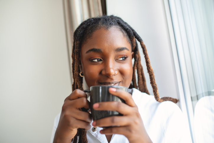 Closeup view of young woman with cup of hot drink at home, blank space. People, drinks and leisure concept - happy young woman with cup of tea or coffee at home