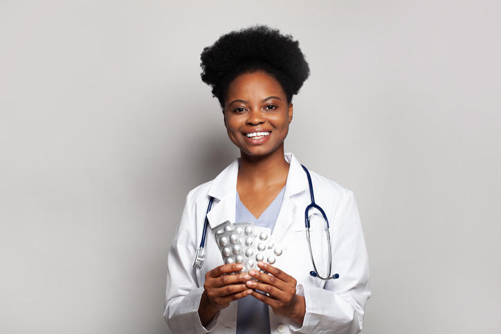 Friendly doctor woman holding pill tablet on white background