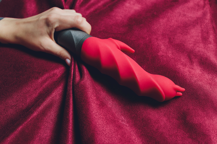 Woman in bedroom holding vibrator in hand.