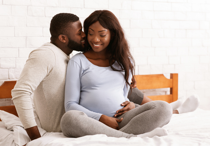 Cheerful young pregnant couple cuddling in bed at home