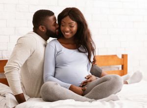 Cheerful young pregnant couple cuddling in bed at home