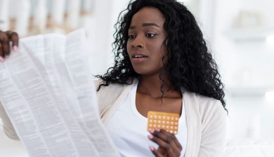 Shocked african american woman reading leaflet before taking contraceptive birth control pills