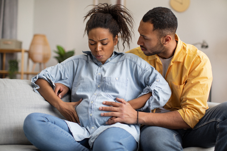 Pregnant African Woman Having Labor Pains, Husband Hugging Her Indoors