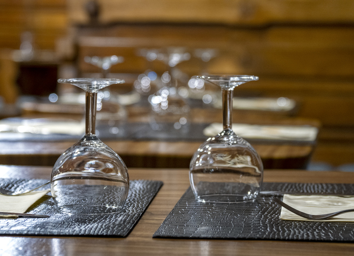 Tables in a restaurant with cutlery and glasses prepared for dinner.