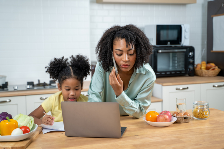 African American mother with daughter working online on computer in kitchen.