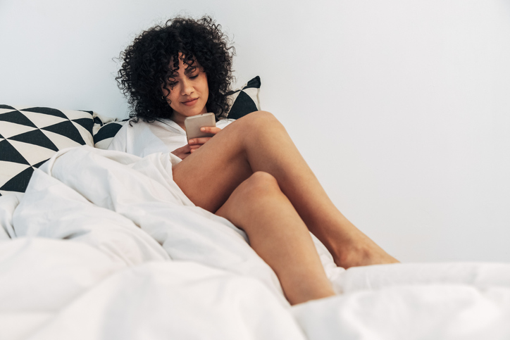 Young mixed race woman looking at social media in bed.