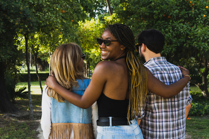 Multiracial group of friends walking in a natural park. Polyamory relationship concept.