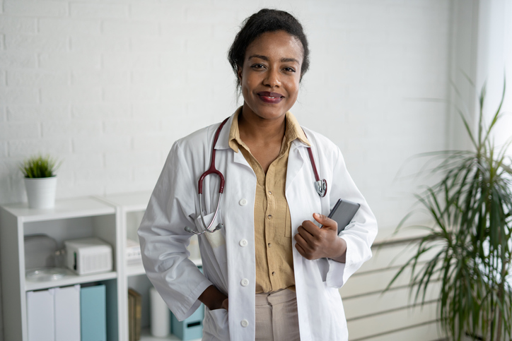 Portrait of a beautiful smiling female African American doctor standing in a medical office. Health care concept, medicine insurance, copy space.
