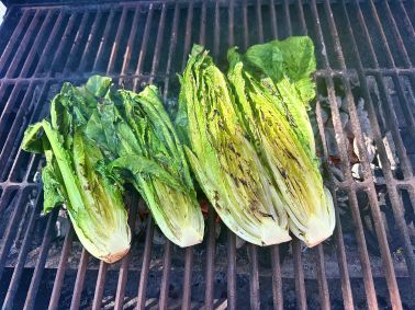 Four pieces of halves of romaine hearts sitting on the grill.  They will be served alongside grilled lobster tails.