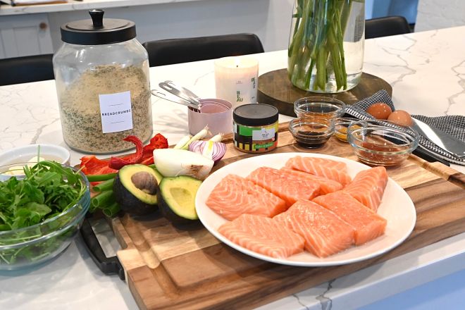 The ingredients for the jerk salmon burger laid out on a kitchen counter, including fresh salmon, avocados, herbs and spices.
