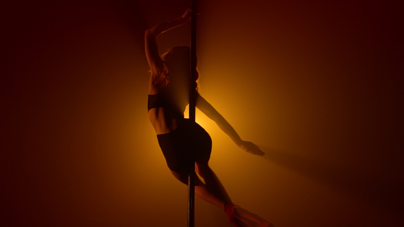 Sexy silhouette performing erotic dance on strip pole. Woman dancing sensually.