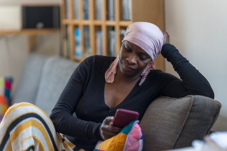 Woman wearing a pink headscarf with cancer consults the messages on her phone