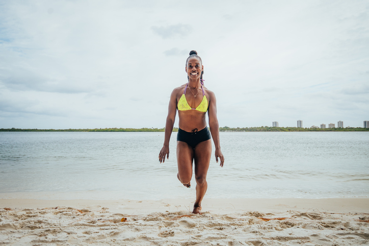 Beautiful young African American woman, competitive fitness model and athlete, running for exercise on an idyllic beach