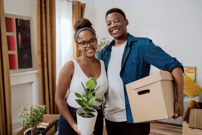 Students getting ready to leave for college couple in love packing things in cardboard boxes carrying them out of house woman holding plant in hands to take away mutual help during moving out