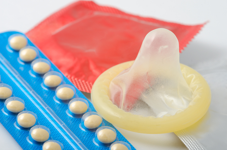 Close-Up Of Condom And Pills Over White Background