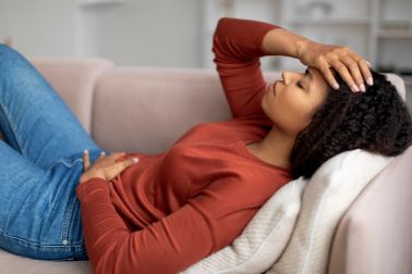 Sick black woman lying on couch, feeling unwell at home