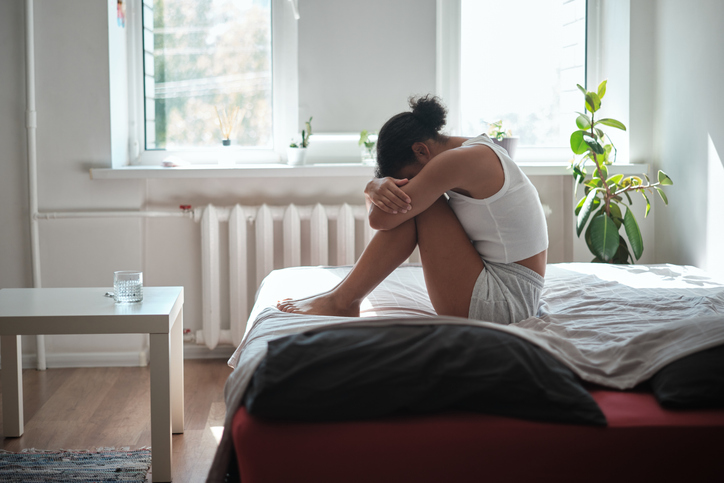 Sad depressed African American woman sitting on bed hugging knees, crying feeling upset. Mental health, depression