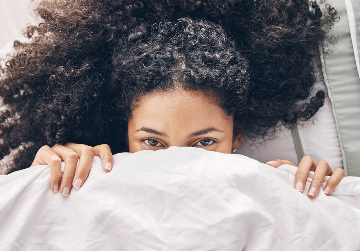 Above bed, portrait and black woman in the morning after sleep rest and relaxing at home with blanket. Eyes, house and wake up happiness of a young person hiding face under the bedroom covers