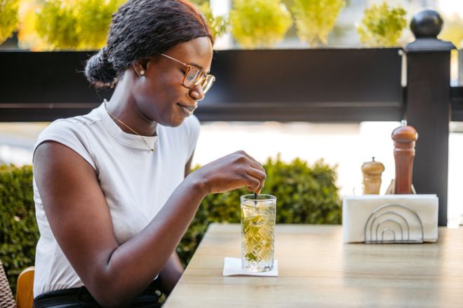 Young Black Woman Drinking A Mojito Cocktail In A Bar Outdoors