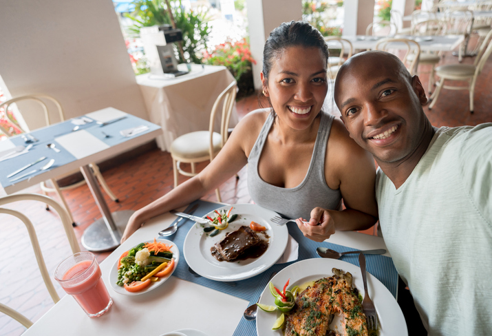 Latin american diverse couple on their vacation enjoying lunch and taking a selfie looking at camera smiling