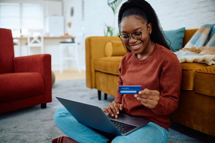 Happy black woman using credit card while shopping online at home.