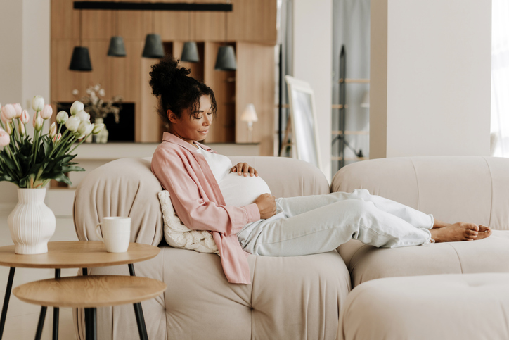 Pregnant woman relaxing on sofa is touching her belly