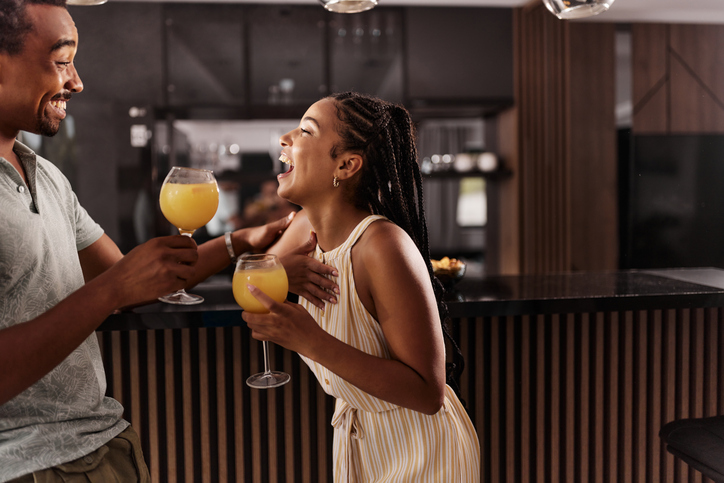 Cheerful black couple talking while drinking juices at home.