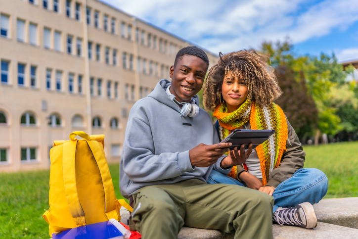 Diverse students smiling while using tablet outside the university