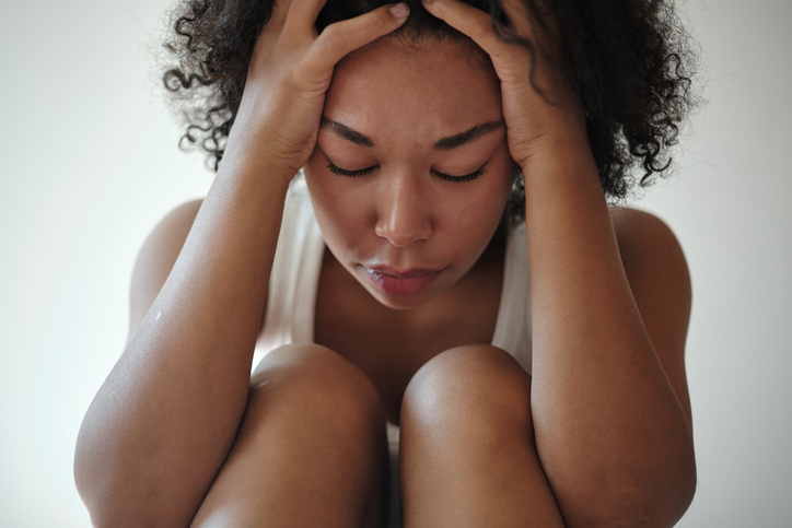 Frustrated African American woman sitting on bed holding head in hands suffering from headache, feeling depressed