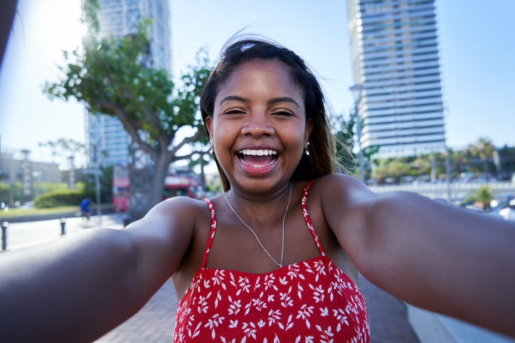 Beautiful young African American woman taking selfie outdoors in the city beach.