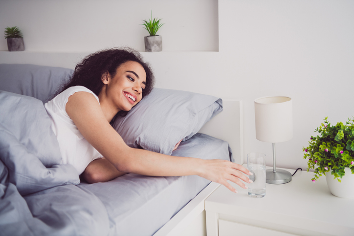 Photo of charming young woman lying bed wake up drink water glass good morning vibes awake home bedroom light white interior
