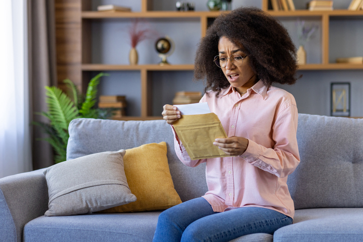 Woman sitting on sofa feeling surprised while reading a letter