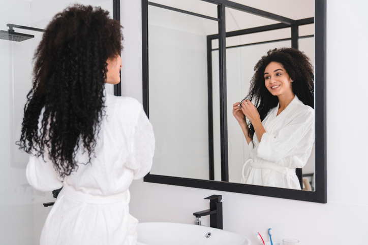 Young african woman in white bathroom after taking shower bath taking care of her curly hair