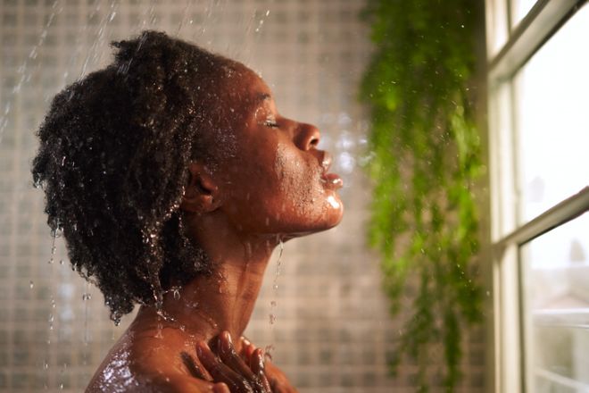 Headshot of an African woman in the shower relaxing with the water running in her face.