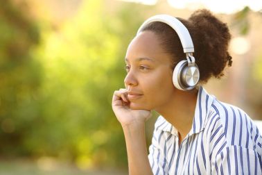 Relaxed black woman in a park wearing headphone looks away